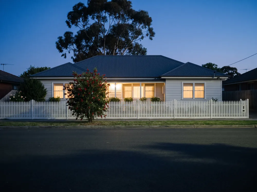 A weatherboard house at dusk with every window lit